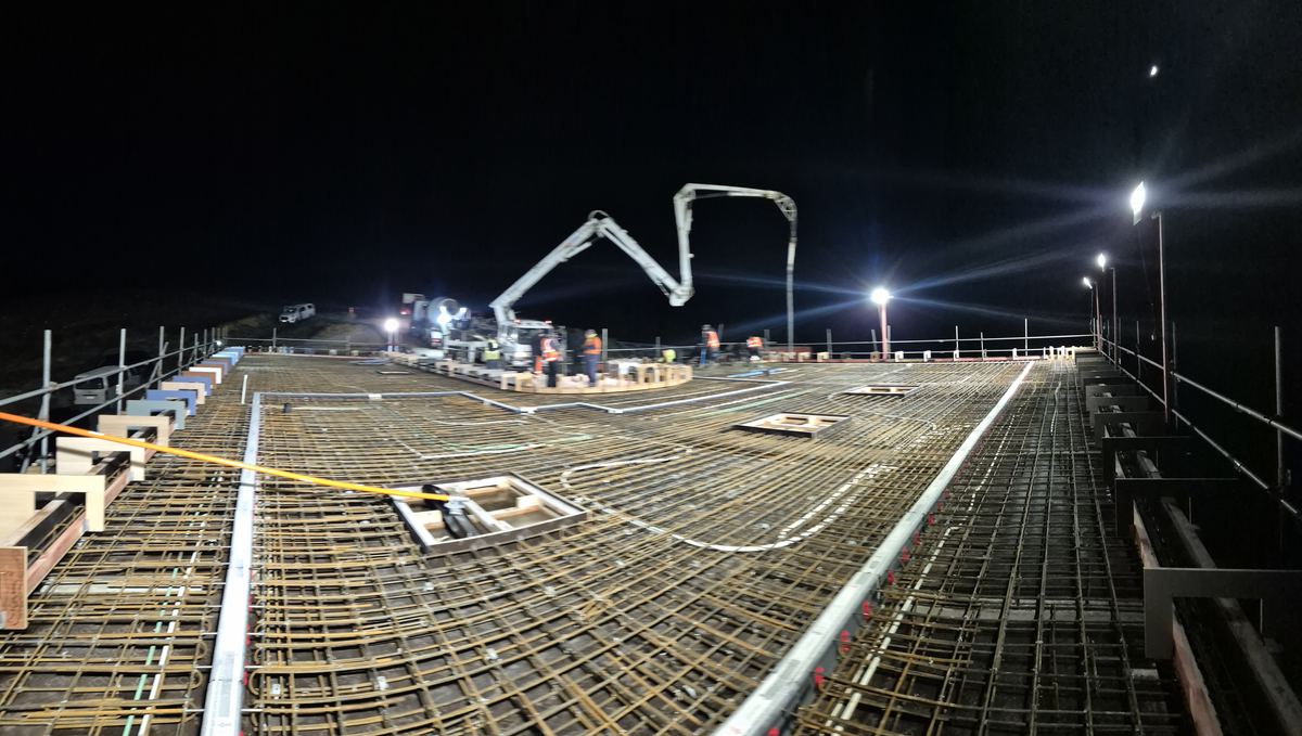 Concrete pump placing concrete over steel reinforcing at night